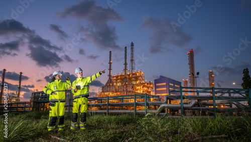 Cuadro en lienzo discuss refinery workers engineers petroleum team talking engineer in high visibility safety gear inspect brightly lit at dusk highlighting energy operations and fuel industrial infrastructure