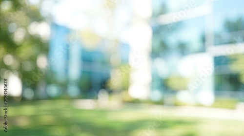 Blurred outdoor background of a modern office building with green lawn on a sunny day.