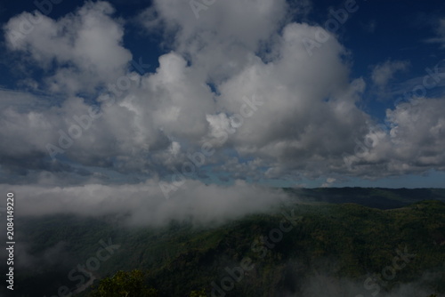 A breathtaking panoramic landscape featuring towering white cumulus clouds drifting above a lush green mountain valley.