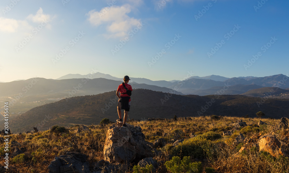 Obraz premium An 11-year-old boy with an arm brace stands on a rock, looking at mountain panorama in Crete. Inspiring travel of youth adventure, achieving goals, and overcoming physical injury during holidays