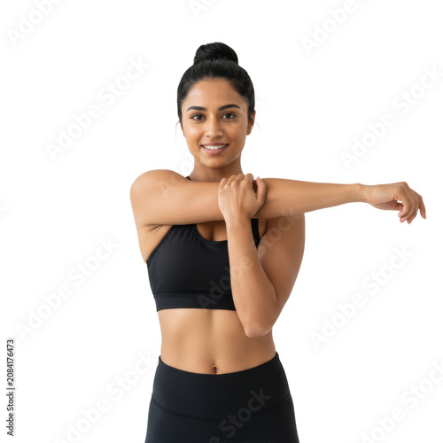Young adult south asian woman with a bun in black athletic wear performing an arm stretch in soft lighting against a white studio wall concept of health and fitness