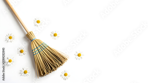 A traditional broom surrounded by scattered white daisies on a clean background evokes a sense of freshness and spring cleaning.