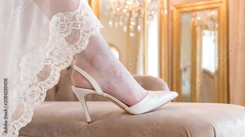 Close up of bride foot in elegant white high heels and lace wedding dress preparing for marriage ceremony