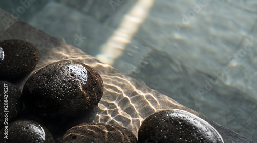 Sunlight reflecting on water surface with zen basalt stones in luxury spa pool background
