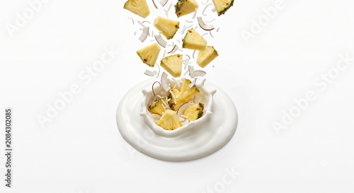 Distant shot of pineapple chunks and coconut flakes falling into thick white yogurt cream