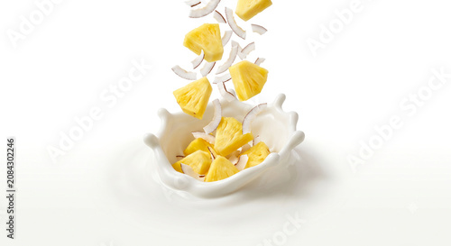 Distant shot of pineapple chunks and coconut flakes falling into thick white yogurt cream