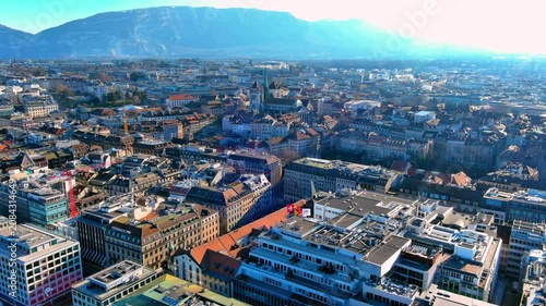 Aerial view of Geneva city center, Switzerland, with the Rue du Rhone district, old town rooftops, St Pierre Cathedral and the Saleve mountain in the background on a clear winter day.