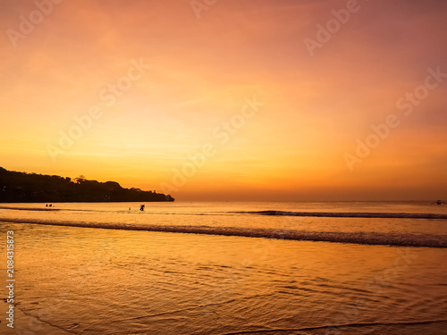 Sunset over Jimbaran Beach with silhouetted figures on shoreline, Bali, Indonesia