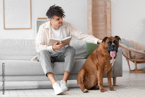 Young man with Boxer dog reading book on sofa at home