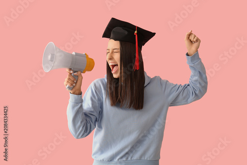 Young female graduate megaphone on pink background
