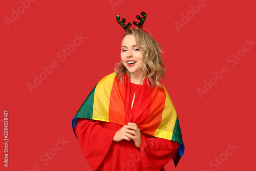 Beautiful young woman in reindeer horns with LGBT flag on red background. Chr...