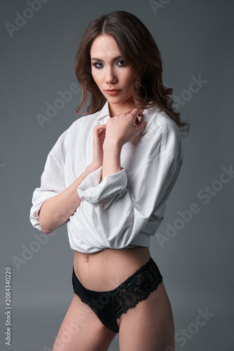Studio portrait of sexy young woman. Beautiful girl dressed in underpants and male shirt. Sensual lady against gray background