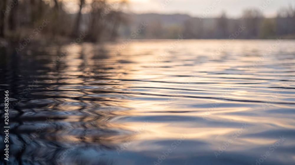 Αυτοκόλλητο Gentle water ripples reflecting sunset light on a calm lake