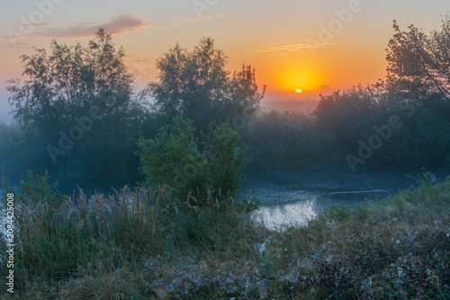 Fotografía The golden sun rises over a misty river landscape, casting a warm glow on the lu