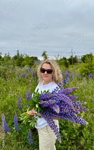 Blonde in sunglasses holds a bouquet of blue lupines in her hands
