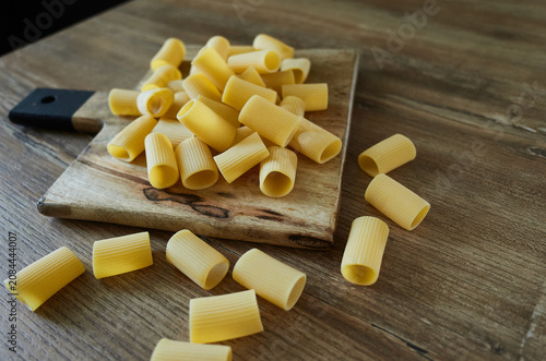 Freshly shaped pasta placed on a wooden cutting board with some pieces scattered on the table