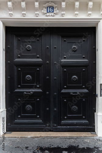 Classic black double wooden door with decorative metal studs and floral motifs, set in a white stone building facade.