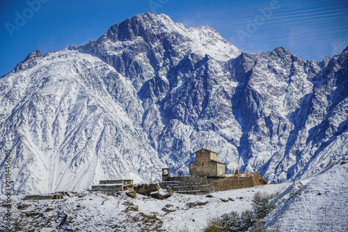 Canvastavla Ancient Gergeti Trinity Church and towering snow-capped Mount Kazbek under clear blue sky, Stepantsminda, Georgia