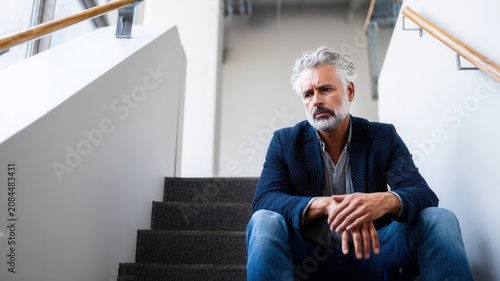 Mature man feeling stressed looking down with disappointment while sitting on office stairs alone