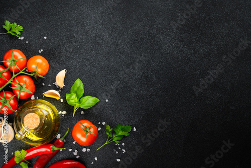Fresh tomatoes, basil, rosemary, spices and olive oil bottle on black table.