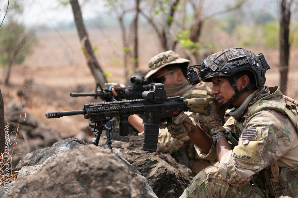 Fototapeta premium Military personnel take position behind rocks during an exercise in a forested area in the daytime