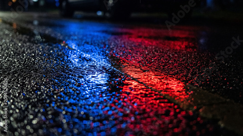 Red and Blue Emergency Vehicle Lights Reflecting on Wet Asphalt Street Night Background
