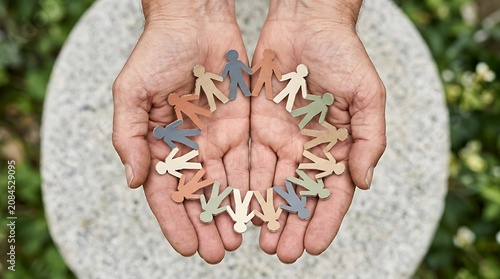 A pair of hands holding a circular group of diverse paper cutout people figures representing community support unity and global human connection