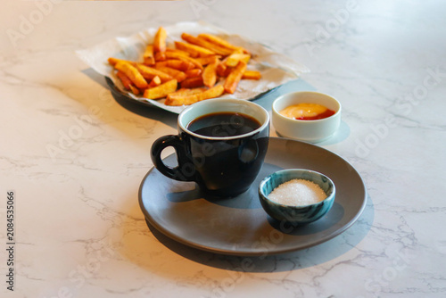 Black Coffee in Ceramic Cup Served with Sugar and Crispy French Fries on Marble Table