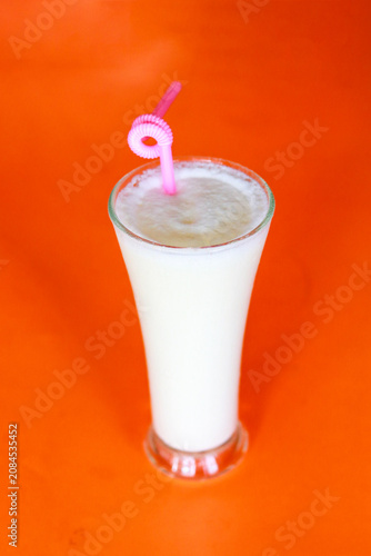 Refreshing Sweet Lassi Yogurt Drink in Glass with Pink Straw on Vibrant Orange Background