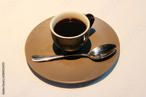 Hot Black Coffee in Elegant Ceramic Cup with Spoon on Saucer Against Light Background