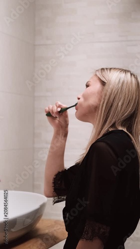 Morning routine: A beautiful blonde brushing her teeth in the bathroom. Side view.
