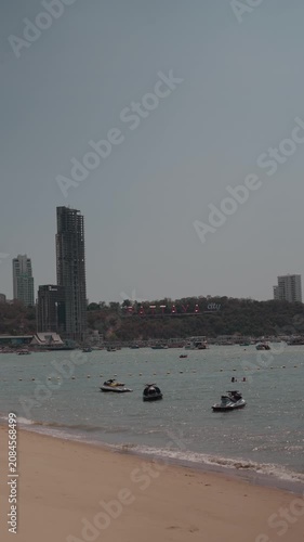 Pattaya, Thailand - Scenic daytime Pattaya Beach featuring calm turquoise water, anchored boats, and the modern city skyline.