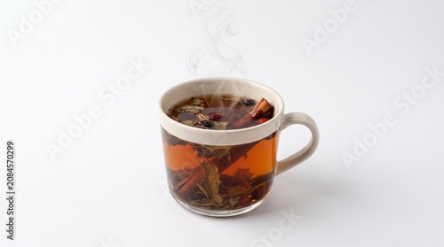 Steaming mug of herbal tea with cinnamon sticks and berries on white background