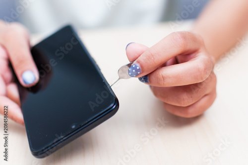 Close up view of a hand carefully taking out a sim card from a smartphone on a light wooden table
