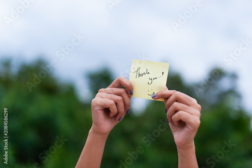Joyful individual holding a thank you note surrounded by a serene natural backdrop smiling warmly