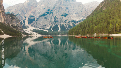 Fotografie Lake braies reflecting alps mountains and moored wooden boats