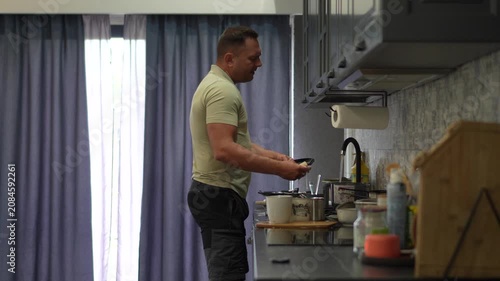 A cheerful adult man singing passionately into a kitchen knife like a microphone while cooking and dancing in a modern kitchen.