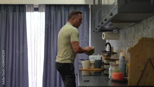 A happy adult man dancing enthusiastically while doing the dishes in a modern kitchen at home.