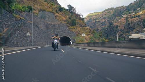 Biker riding motorcycle on mountain road entering tunnel