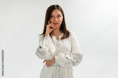 Thoughtful young woman in traditional Ukrainian embroidered dress (vyshyvanka) posing on white background. Ethnic fashion, culture, and national identity concept