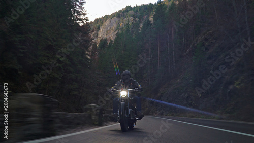 Biker riding motorcycle on winding mountain road through forest