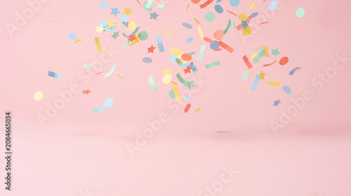 Colorful party confetti falling on a soft pastel pink background with copy space for celebration text