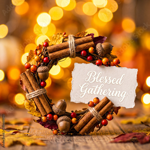 Autumn wreath with cinnamon sticks, acorns, and berries with a blessed gathering sign on a wooden table