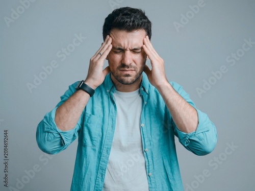 Close up of man in blue shirt holding head showing distress from severe headache