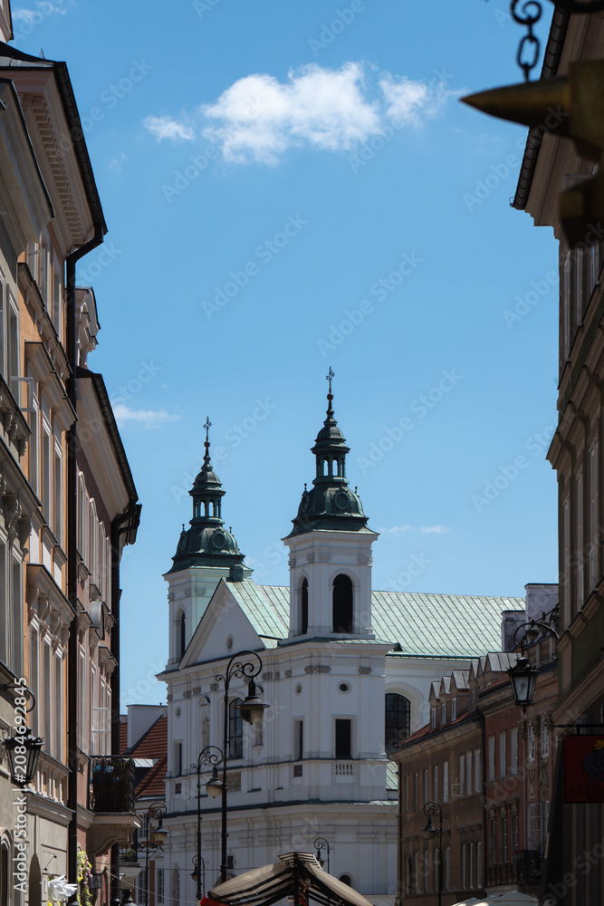 Fototapeta premium Historic church towers stand at old town street city landmark. Ancient European architecture building facade represents Poland history heritage site tourism and summer travel destination.
