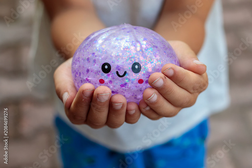 Canvas Print Smiling little boy playing with a glittery dumpling shaped squishy toy outdoors,