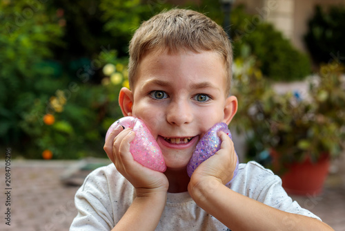 Bild auf Leinwand Smiling little boy playing with a glittery dumpling shaped squishy toy outdoors,