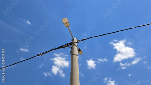 Concrete utility pole with a street light and overhead power lines against a blue sky