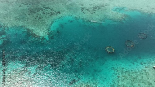 Turquoise coral reef waters with visible fish cages and a small boat crossing nearby. Siargao, Philippines.