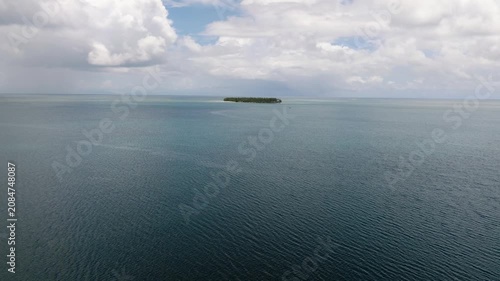 Isolated small island covered with trees surrounded by calm ocean waters and cloudy horizon. Siargao, Philippines.